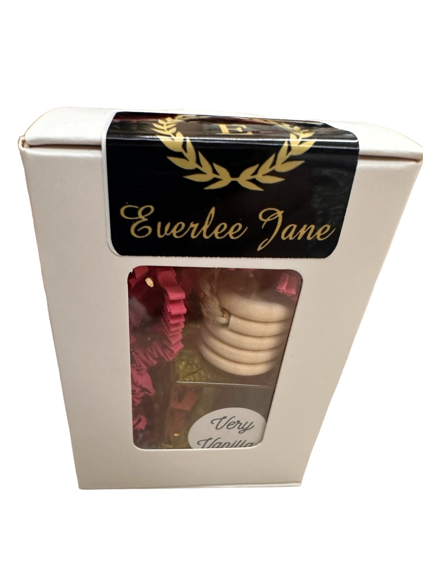 White box with clear window displays Car Diffusers labeled "Very Vanilla." Black and gold label at the top reads "Everlee Jane" with a laurel wreath design. Inside, red decorative elements. Available sizes: Standard.