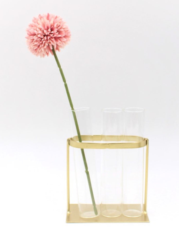 This product is a single pink dahlia, elegantly situated in a 4.5x2.75x6” Glass Vase. The vase is beautifully held by a stylish gold stand, giving the product an overall sophisticated look. It comes with a clean white background which further highlights its charm and elegance.