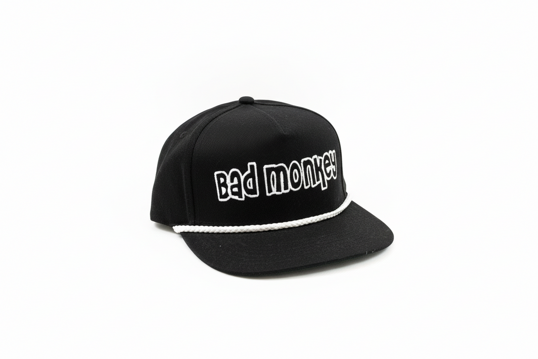 Black adjustable "Bad Monkey" hat with white rope above brim; bold white front lettering. Available in one size fits most.