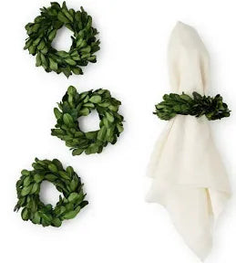 Three small green preserved Boxwood Wreath Napkin Rings and one white cloth napkin in a rustic design.