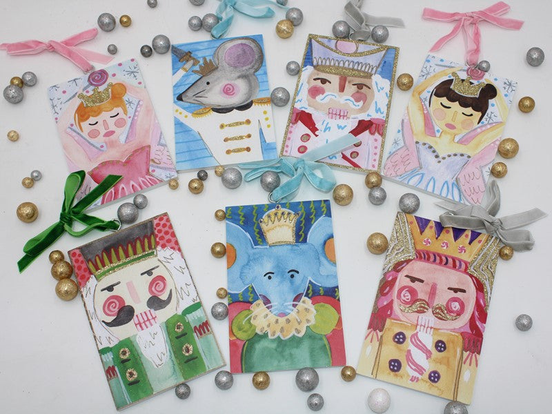 Seven Nutcracker Suite wood ornaments with glitter, 7 styles, rectangular, depicting ballet characters, each with a ribbon loop.