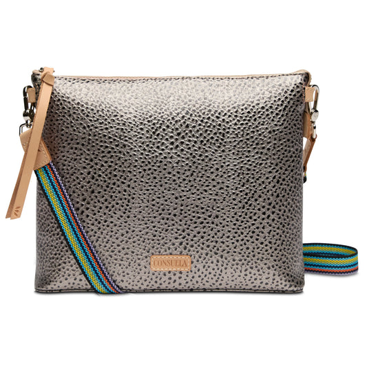 The Downtown Crossbody by Tommy has a metallic silver textured finish, multicolored striped adjustable strap, tan leather accents, and a small rectangular leather patch with embossed text on the front. Sizes available: Small, Medium, Large.
