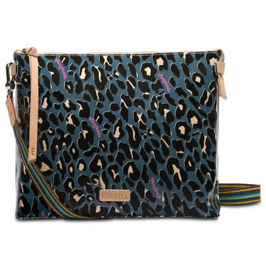 **Danni Downtown Crossbody**: Stylish crossbody bag with leopard print and small pink text. Features a brown leather label and adjustable multicolored striped shoulder strap. Made from durable ConsuelaCloth™. Sizes available: One size fits all.