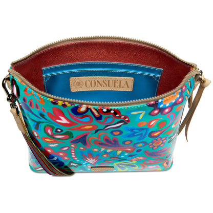 The Downtown Crossbody, Tasha is a colorful floral-patterned ConsuelaCloth shoulder bag with a zipper closure, adjustable strap, blue inner pocket with tan “Consuela” label, and shimmering red lining. Available sizes not specified.