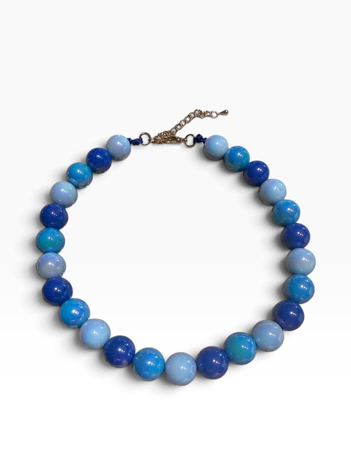 Blue beaded necklace with round stones, metal clasp, and chain extender. Available in multiple sizes.