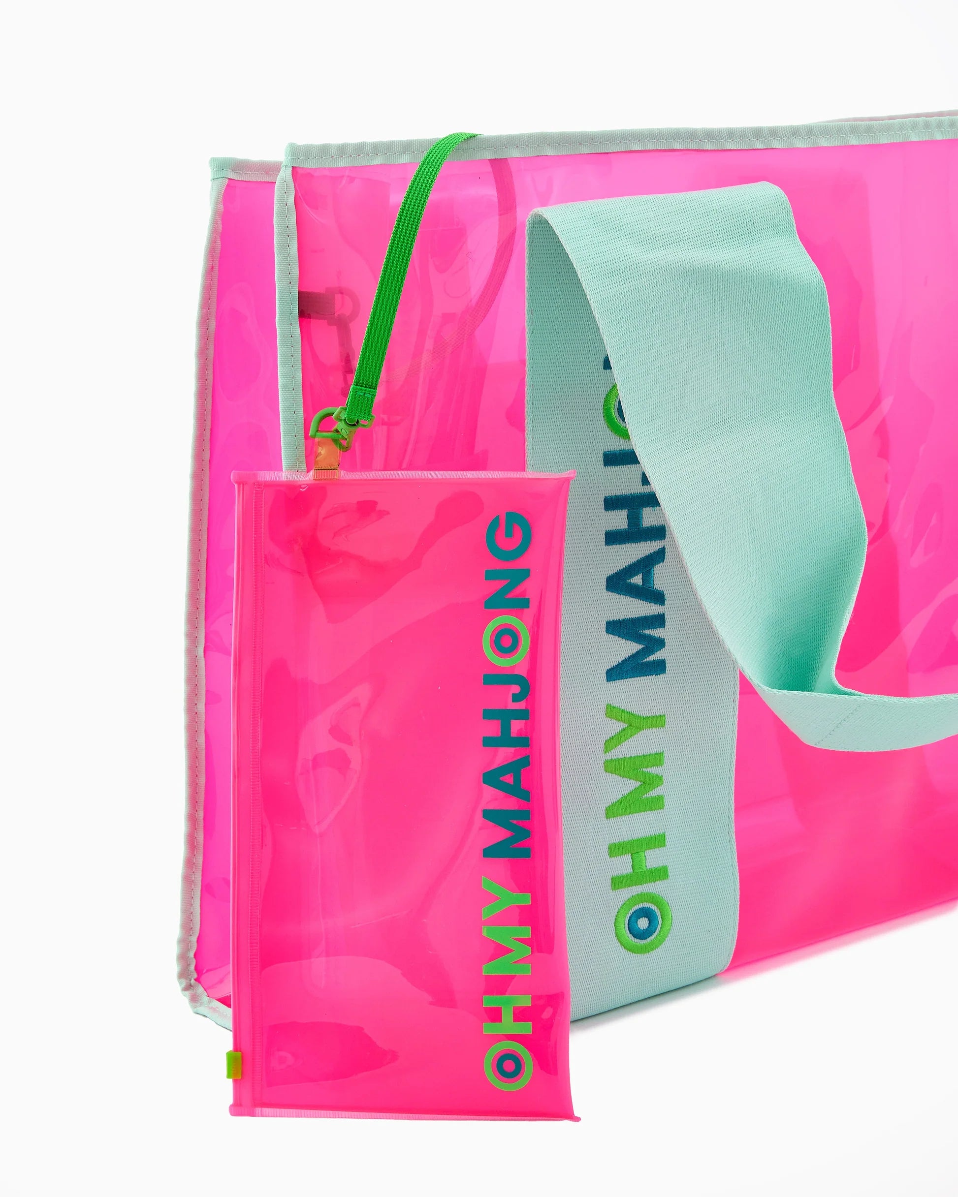 Mahjong Beach Bag: vibrant pink transparent tote with light blue handles and attached pink zip pouch, both labeled "OH MY MAHJONG" in bold, colorful text. Available sizes: standard.
