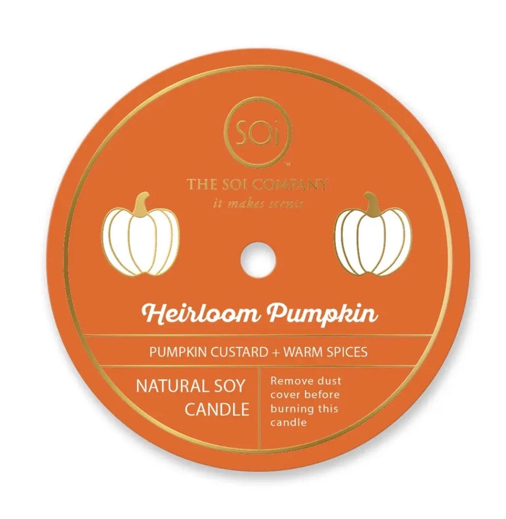 Round orange label with gold trim, two white pumpkins, and text: “Heirloom Pumpkin 12oz Icon Candle,” “Pumpkin Custard + Warm Spices,” “Natural Soy Wax Candle,” and dust cover removal reminder. Available in 12oz size.