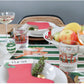 A festive holiday table setting includes:
- Green and white striped table runner.
- Glasses with red reindeer prints.
- Baby Bowl Pinstripes with assorted fruits.
- Loaf of bread.
- Champagne glasses with pomegranate seeds.
- Red stocking-shaped name card with greenery.

Sizes:
Baby Bowl Pinstripes available in: Small, Medium.