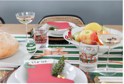 A festive holiday table setting includes:
- Green and white striped table runner.
- Glasses with red reindeer prints.
- Baby Bowl Pinstripes with assorted fruits.
- Loaf of bread.
- Champagne glasses with pomegranate seeds.
- Red stocking-shaped name card with greenery.

Sizes:
Baby Bowl Pinstripes available in: Small, Medium.