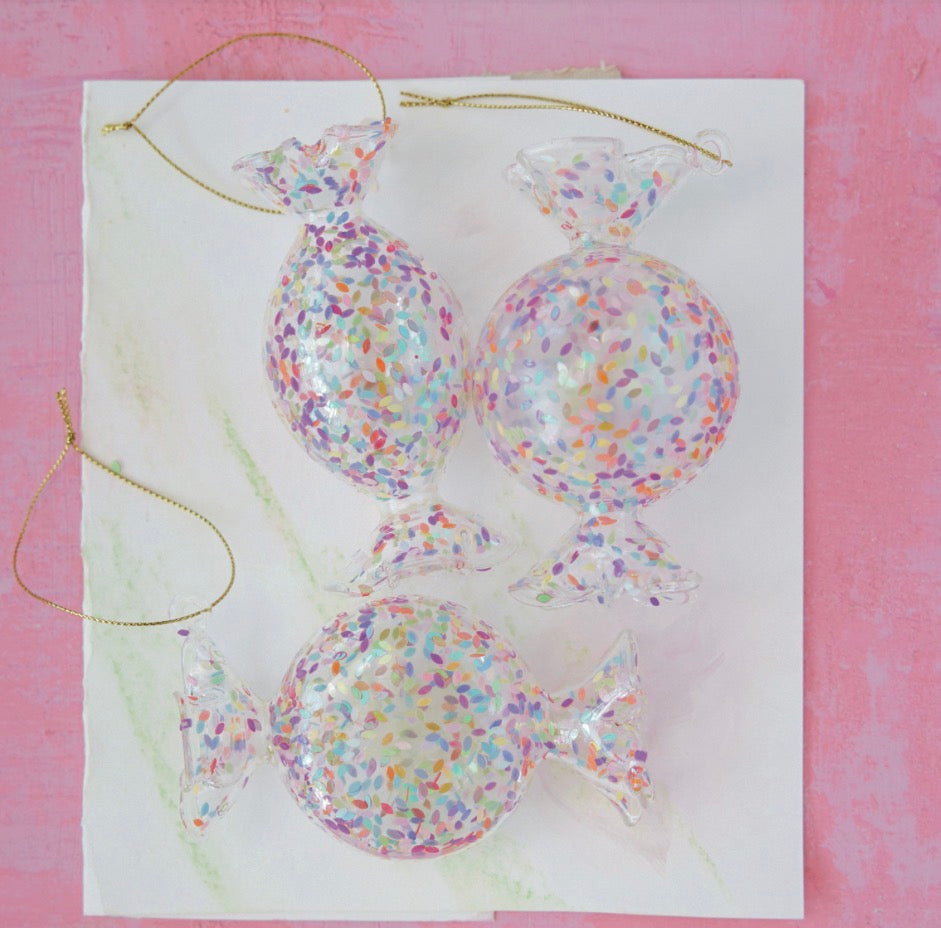 Three candy-shaped confetti glass ornaments with gold hanging strings.