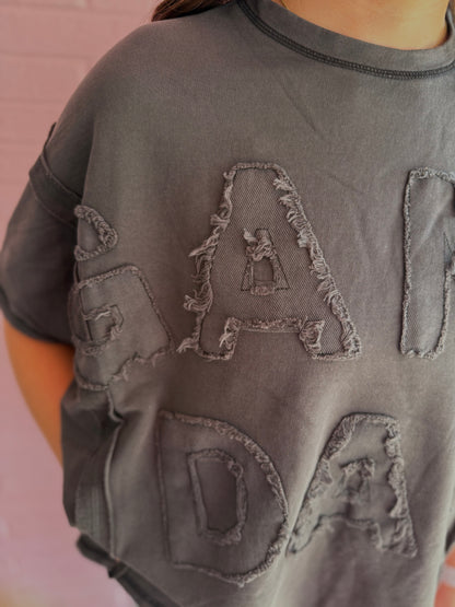 Dye & Wash Gameday Terry Top in dark gray, made from soft French terry with large frayed fabric letters and a unique dye and wash finish. Available in sizes XS–XL.