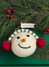 Round white felted wool Snowball Ornament with striped headband, red pom-pom earmuffs, orange nose, and “Tis the season” banner.
