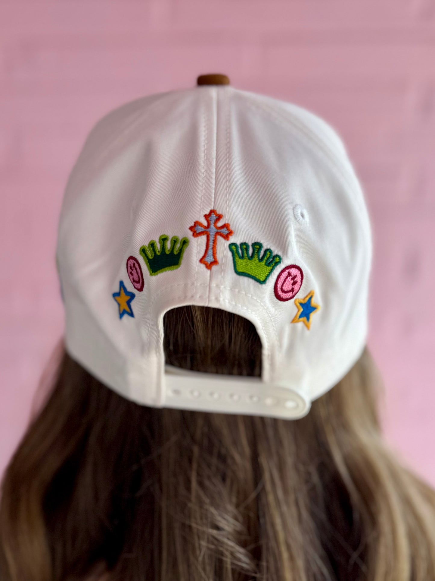 White Love Like Jesus Hat with embroidery of green crowns, red cross, pink smileys, and blue stars. Available in S, M, L.