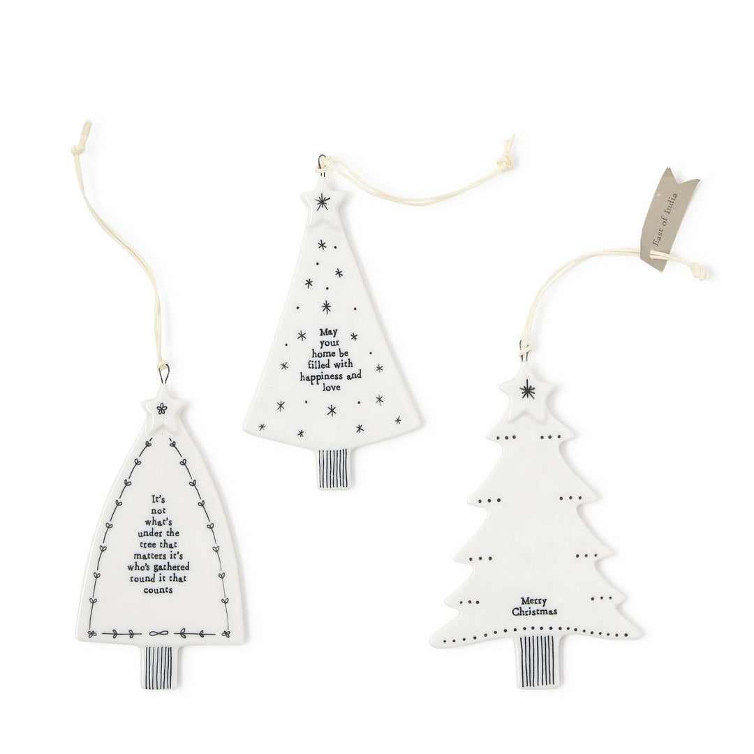 Three white ceramic Christmas tree hanging ornaments with string hangers, black text, and decorative illustrations.