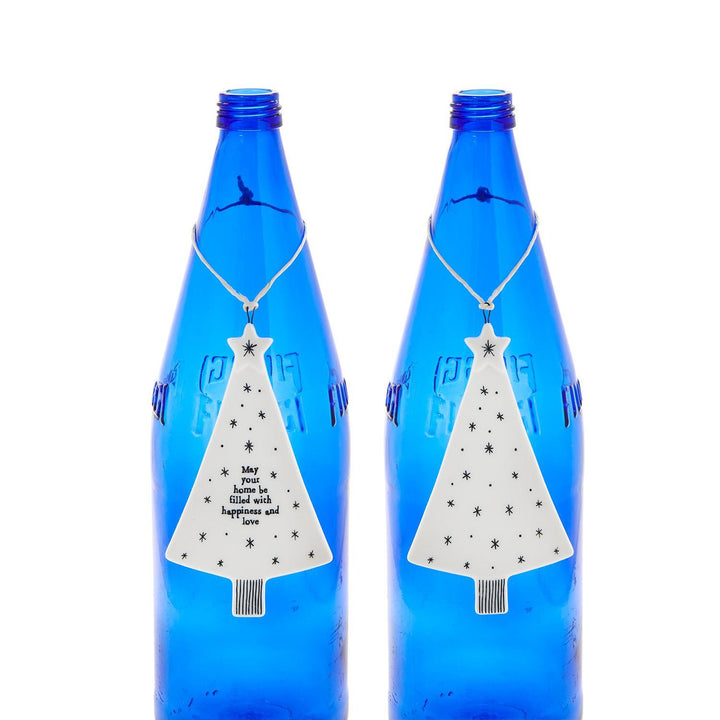 Two white, tree-shaped Christmas ornaments decorated with black stars, one featuring the text “May your home be filled with happiness and love.”.