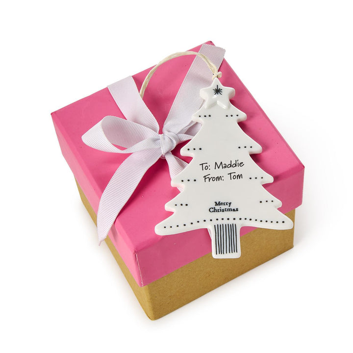White ceramic Christmas tree hanging ornament labeled “To: Maddie From: Tom.”.
