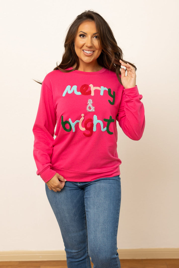 Merry &amp; Bright hot pink relaxed-fit crewneck sweatshirt with multi-colored, textured lettering. Available in all sizes.