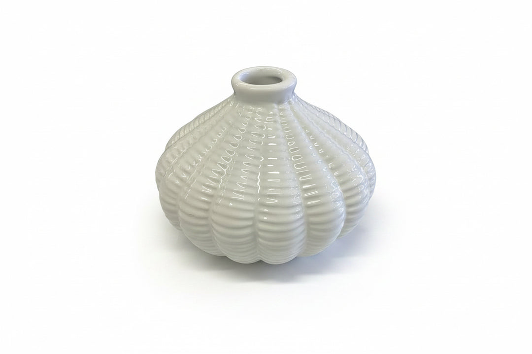 The Artisan Carved Vase is a small, white ceramic vase with a round shape, ribbed texture, and narrow opening. Available in multiple sizes.