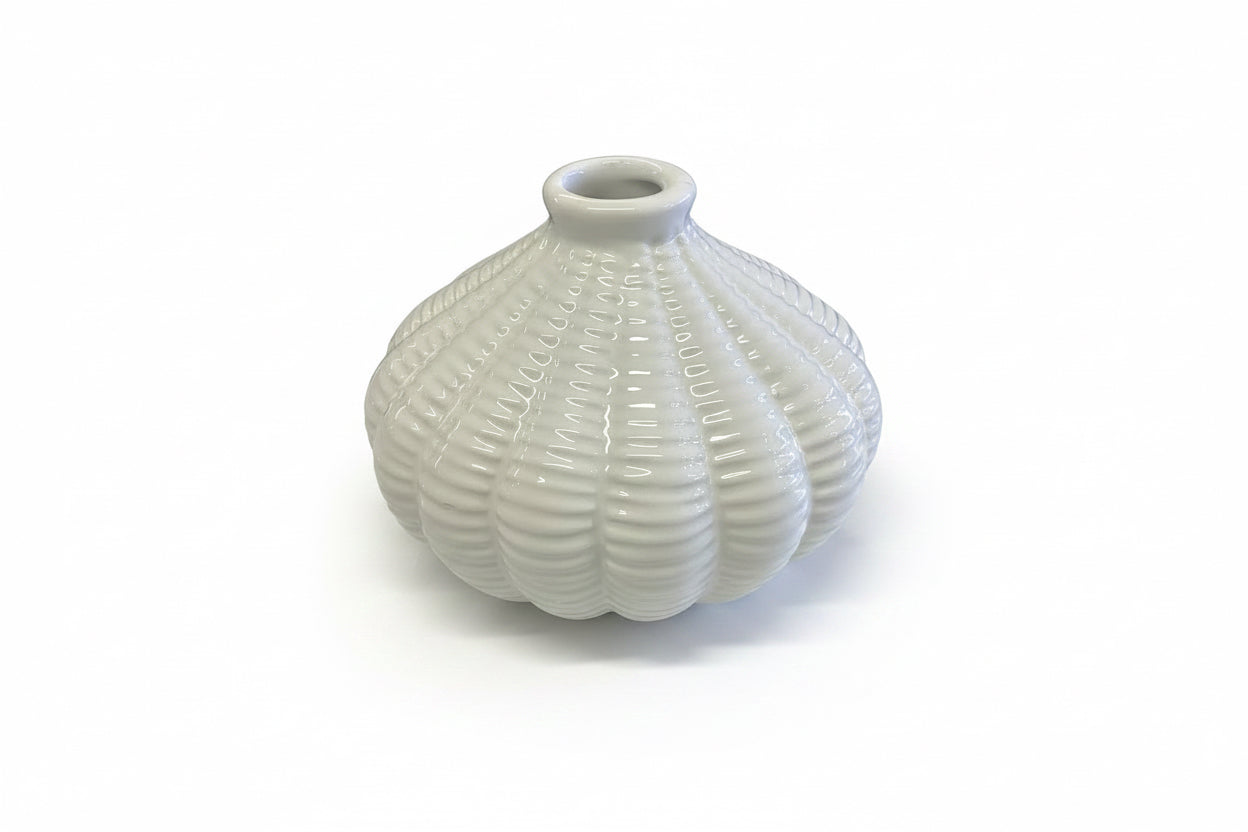 The Artisan Carved Vase is a small, white ceramic vase with a round shape, ribbed texture, and narrow opening. Available in multiple sizes.