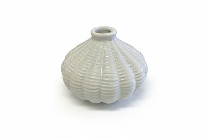 The Artisan Carved Vase is a small, white ceramic vase with a round shape, ribbed texture, and narrow opening. Available in multiple sizes.