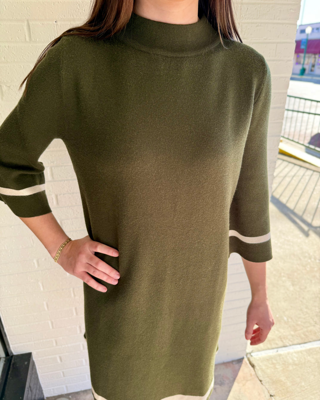 Olive green mock neck sweater dress with three-quarter sleeves and white contrast trim on cuffs and hem. Available in multiple sizes.