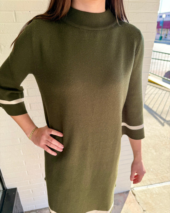 Olive green mock neck sweater dress with three-quarter sleeves and white contrast trim on cuffs and hem. Available in multiple sizes.