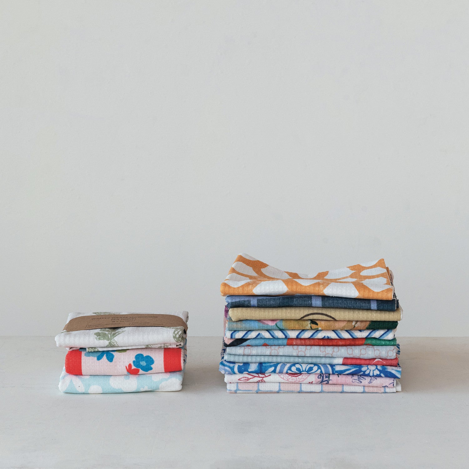 Eco-friendly, absorbent printed microfiber tea towels; available in multiple sizes and colorful designs, neatly folded.