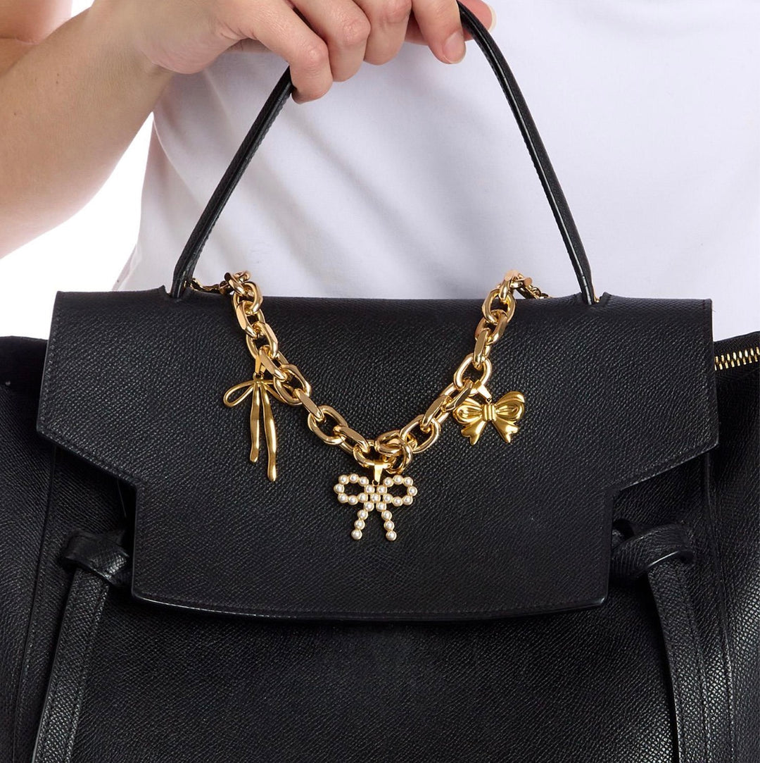 Black textured handbag with Charmed Life Chain Bag Charms: gold chain, bow-shaped charms (one with pearls). Available in small, medium, and large.