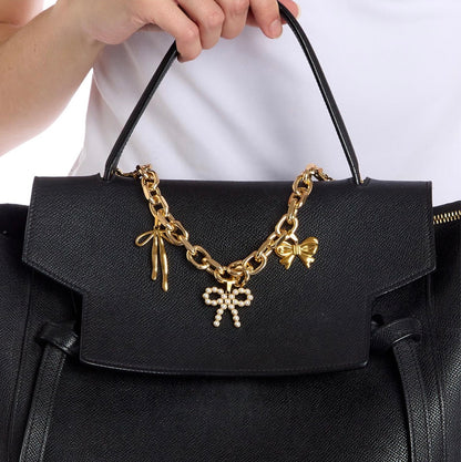 Black textured handbag with Charmed Life Chain Bag Charms: gold chain, bow-shaped charms (one with pearls). Available in small, medium, and large.