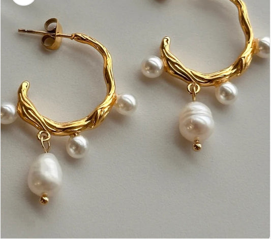 Gold hoop earrings with a textured design and dangling white pearls. Multiple small pearls along the hoop; one larger pearl at the bottom. Elegant and sophisticated look. Available sizes: Small, Medium, Large.