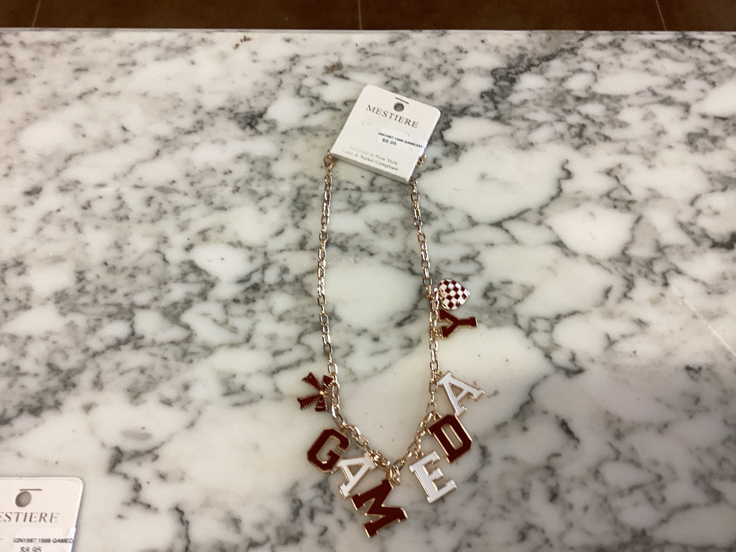 Gold chain necklace with red and white football-themed charms spelling “GAME DAY,” a small red-and-white checkered bead, and an attached Nestiere tag. Available in multiple sizes.