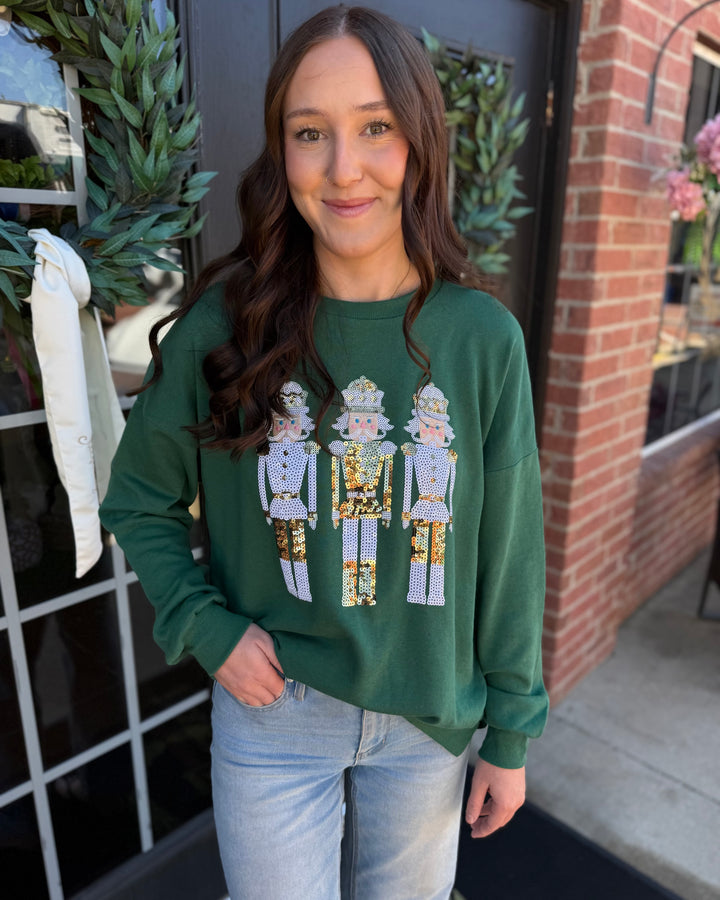 Dark green Alpine Nutcracker sequin sweatshirt featuring three decorative gold and silver sequin nutcrackers. Available in various sizes.