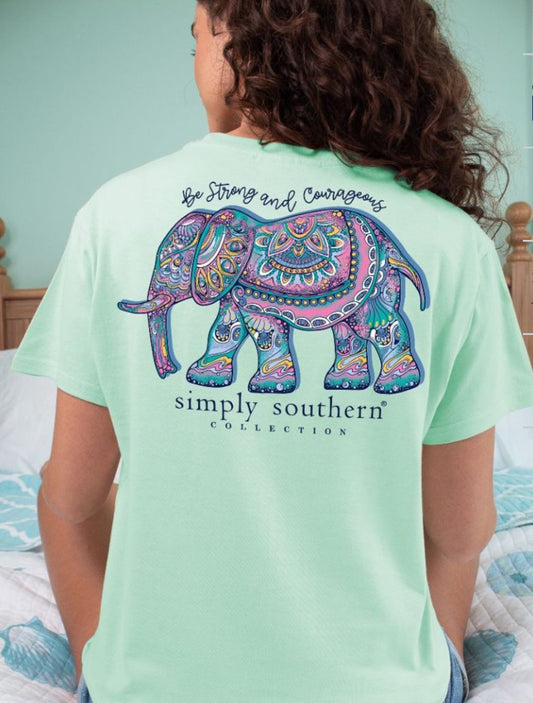 A woman seen from behind, wearing a teal t-shirt with a colorful paisley elephant design and the phrase "Strong Chinchilla" printed on it, includes sizing details.