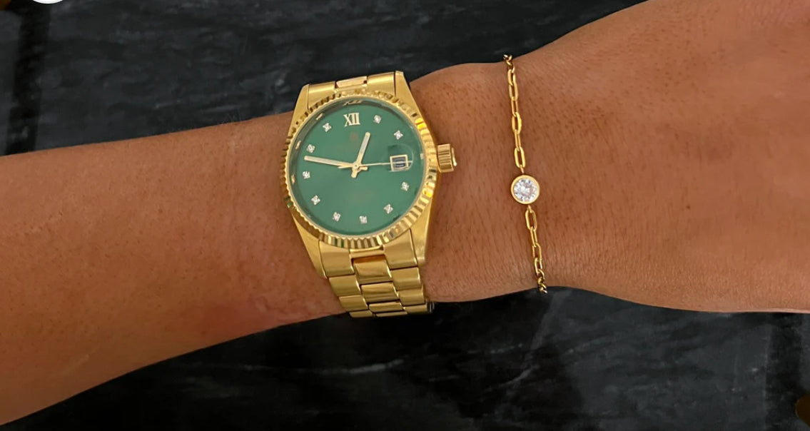 Gold watch with green face, Roman numerals, and diamond markers. Available sizes: small, medium, large. Paired with The Shelby Bracelet featuring a single round gemstone.