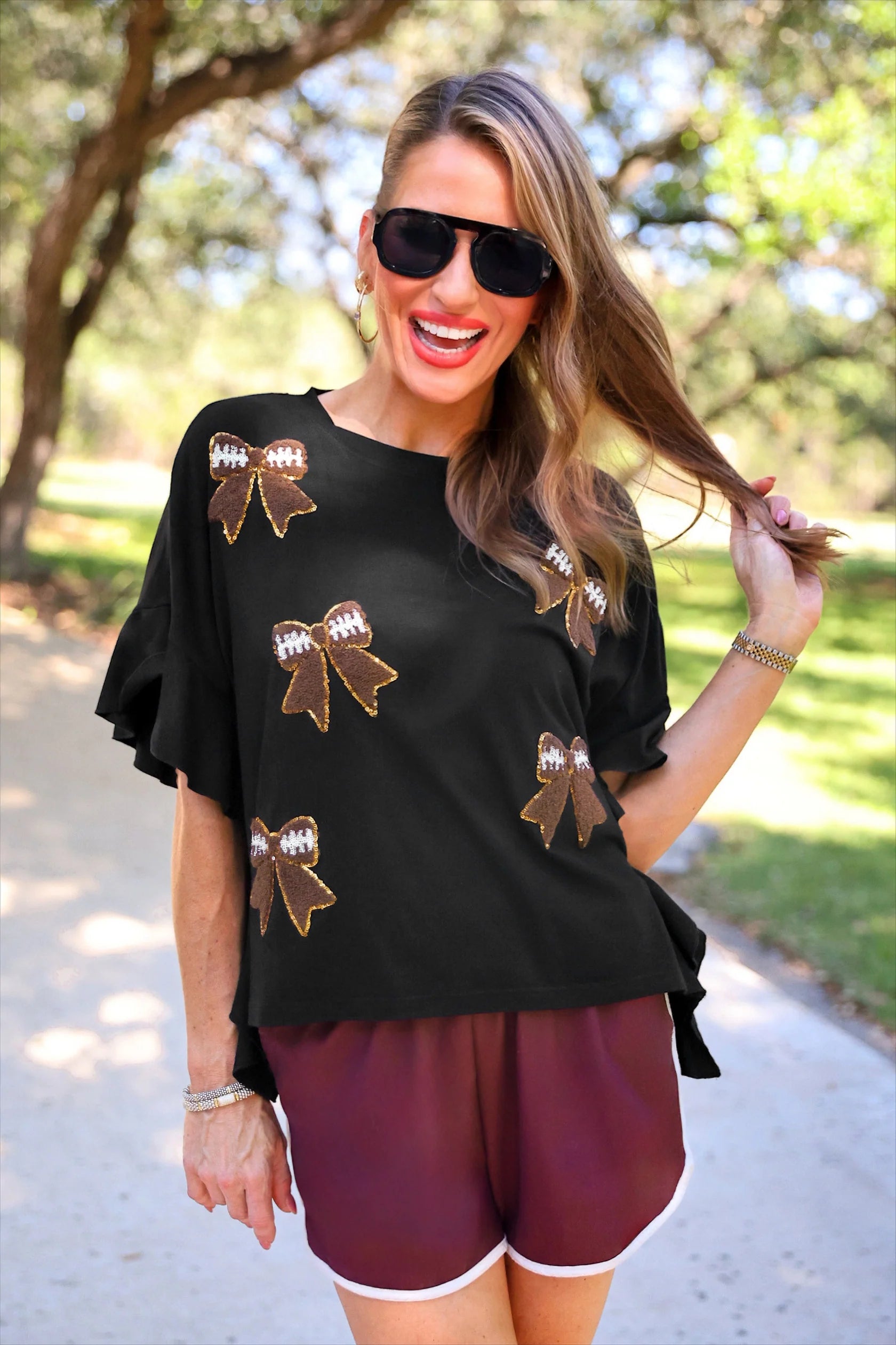 Sideline Sparkle Ruffle Top with gold and brown football bow patches. Available in sizes XS-XL.