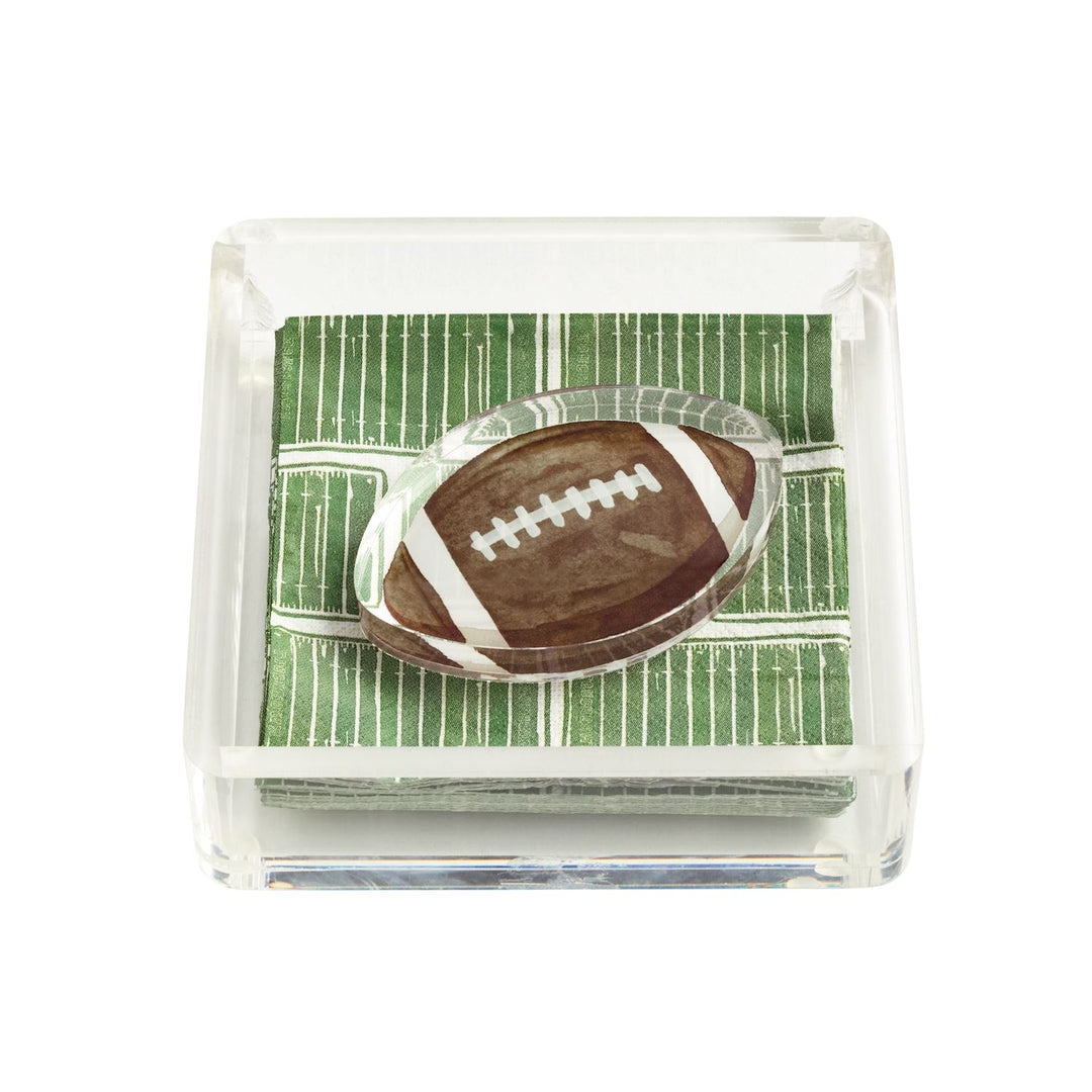 Clear square acrylic napkin caddy with green football-themed cocktail napkins, topped with a small football weight. Sizes available: standard cocktail napkin size.