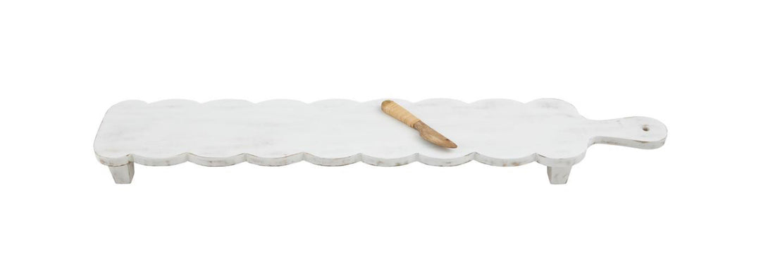 Long, white mango wood cheese board with scalloped edges, short legs. Includes small wooden spreader. Size: Long.