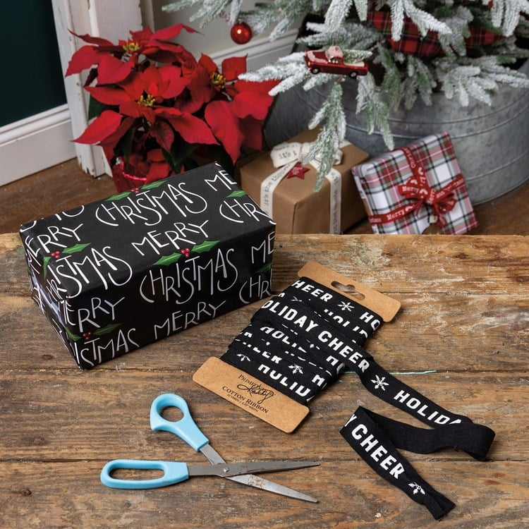 Black Christmas ribbon with white text and snowflake icons on a cardboard spool.
