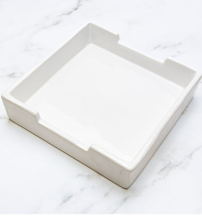 Square white ceramic napkin holder, 5" wide x 3" deep, four side grooves. Available in this size only.