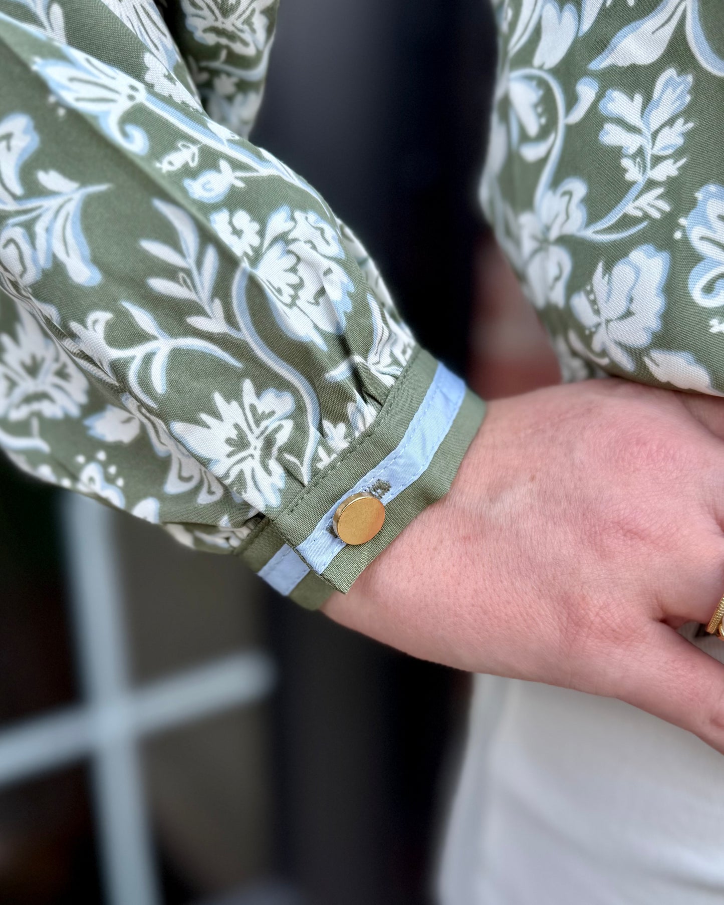 Naomi Painted Trillium Olive Top with floral pattern, light blue cuff, and gold button. Available in sizes XS–XL.