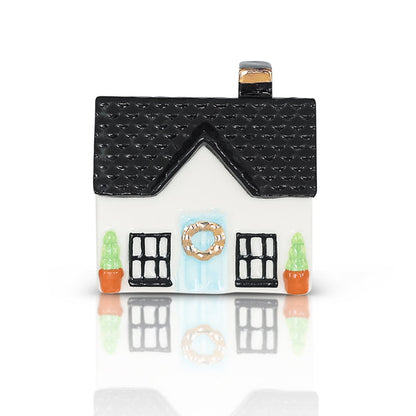 Small ceramic house figurine with black roof, white walls, blue wreath door, and two potted plants; available in one size.