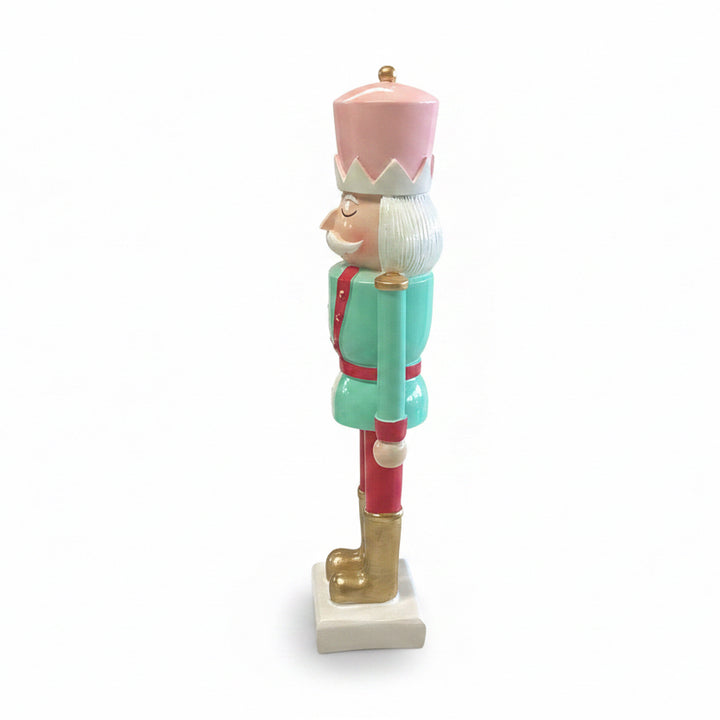 Side view of a Holiday Nutcracker figurine in a pink hat, mint green jacket with red trim, and gold boots.