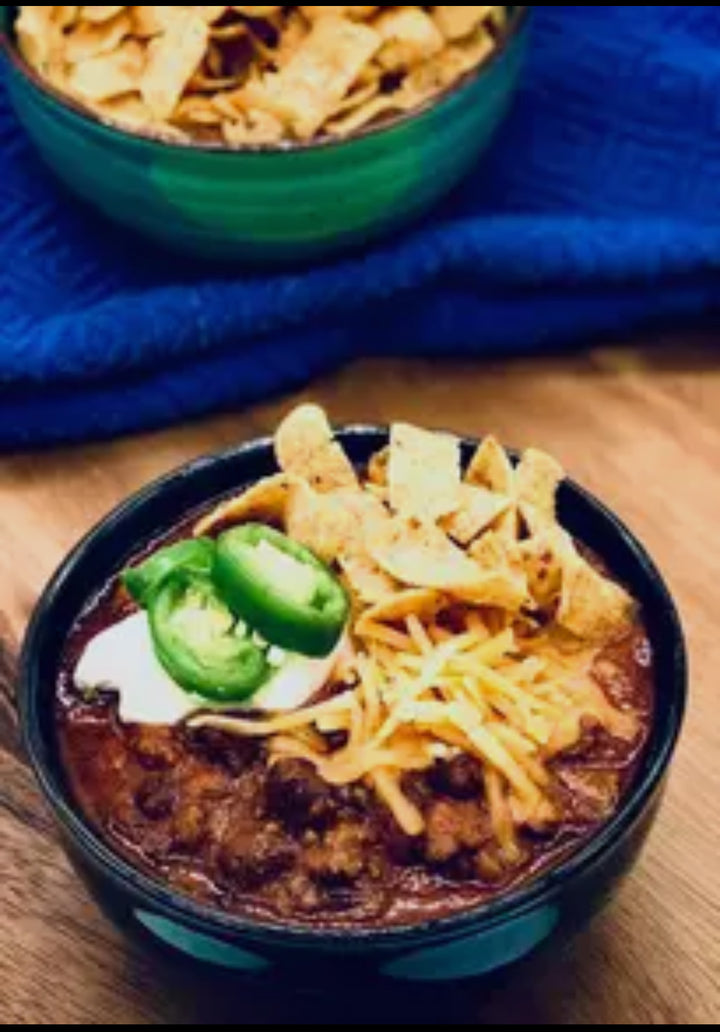 Campfire Chili Soup Mix chili in a bowl, topped with cheese, jalapeños, sour cream, and corn chips. Available in 16oz and 32oz.