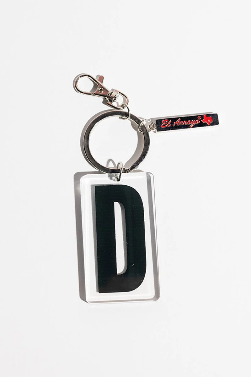 Acrylic keychain, clear rectangle with black "D," metal ring and clasp, black tag with red “El Arroyo” text. Sizes available.