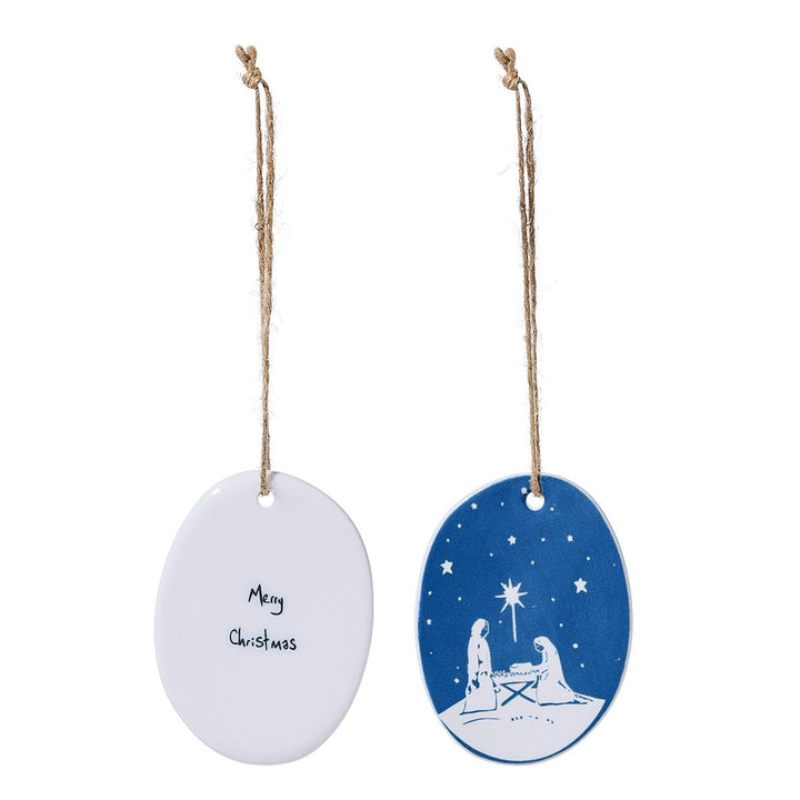 Two oval porcelain ornaments: one white with “Merry Christmas” script, one blue and white nativity scene.