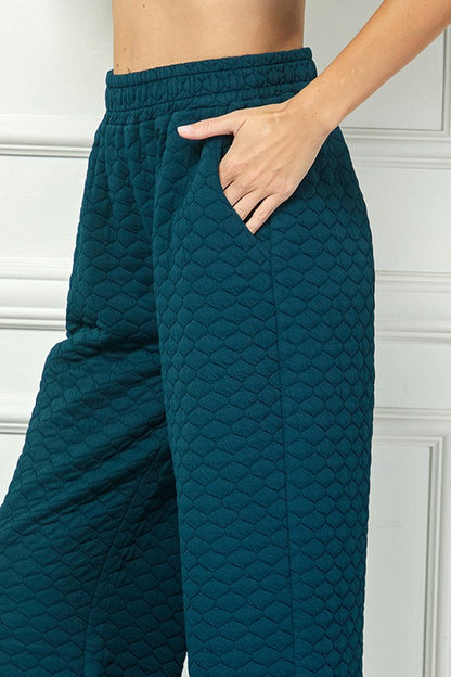 High-waisted teal quilted pants with honeycomb texture. Available in sizes XS–XL.
