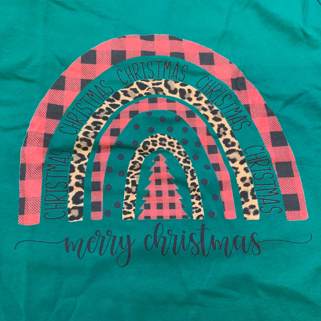 Green Christmas shirt featuring a rainbow arch of red and black buffalo check, cheetah print, and polka dot stripes with “CHRISTMAS” repeated in the arch and “merry christmas” written below.