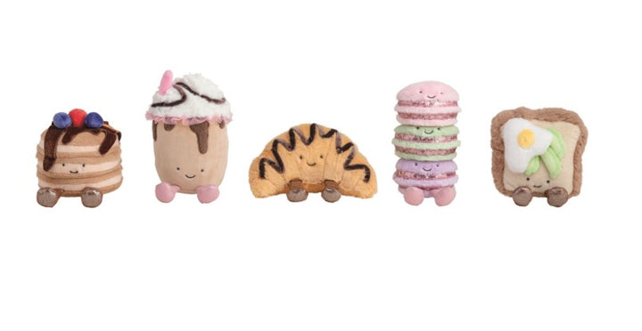 Café Plush Pals featuring five smiling dessert friends: a stack of pancakes, a milkshake, a croissant, three macarons, and a slice of toast with a fried egg. Available in multiple sizes.