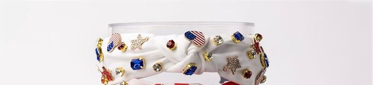 This is a white Americana headband featuring colorful, patriotic-themed charms. The charms include vibrant American flags, stars, and sparkling crystals set against a white backdrop. One size fits all.