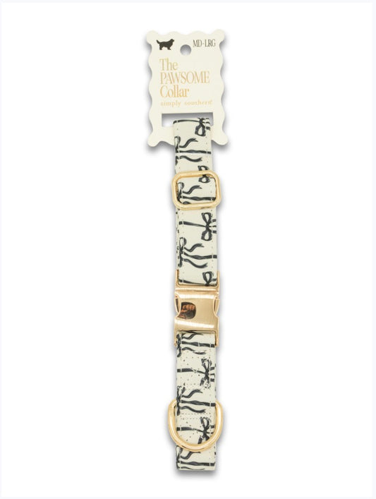 Cream pet collar with black bows, gold hardware, scalloped "The Pawsome Collar" tag. Sizes: XS, S, M, L.